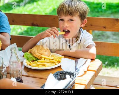 Hamburger gustoso con patatine mangiate da un bambino in una giornata di sole. Foto Stock