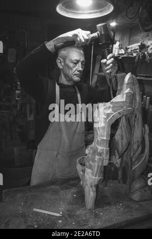 Maestro di legname 50 - 55 anni crea la scultura in legno in officina, la fotografia in bianco e nero Foto Stock