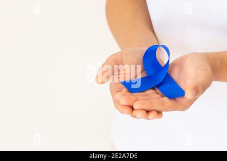 Mani che tengono il nastro blu profondo su tessuto bianco con spazio per la copia. Consapevolezza del cancro colorettale, cancro del colon della persona anziana e giornata mondiale del diabete, Chil Foto Stock