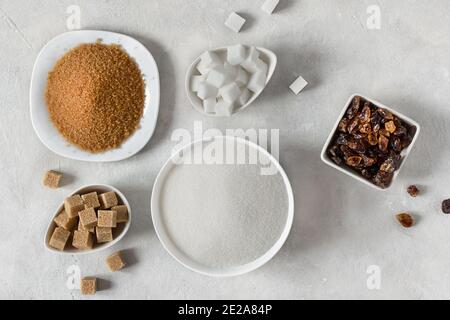 Vari tipi di zucchero. Diversi zuccheri bianchi e marroni in assortimento vista dall'alto su sfondo grigio. Foto Stock