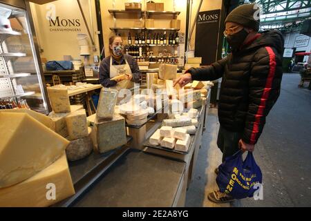 Un acquirente acquista formaggio da Mons Cheesemongers al Borough Market, Londra, che è diventato il primo spazio all'aperto del Regno Unito a imporre legalmente l'uso di maschere facciali per tutti i clienti e gli stallholder. Foto Stock