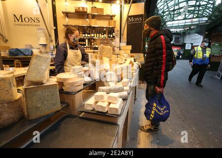 Una guardia di sicurezza passa accanto come un acquirente acquista formaggio da Mons Cheesemongers a Borough Market, Londra, che è diventato il primo spazio all'aperto nel Regno Unito a imporre legalmente l'uso di maschere facciali per tutti i clienti e gli stallholder. Foto Stock