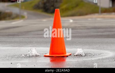 Un cono di strada arancione tra due piccole fontane d'acqua che bolle da buchi nella strada. L'acqua è pulita e pulita. Vista in primo piano. DOF poco profondo. Foto Stock