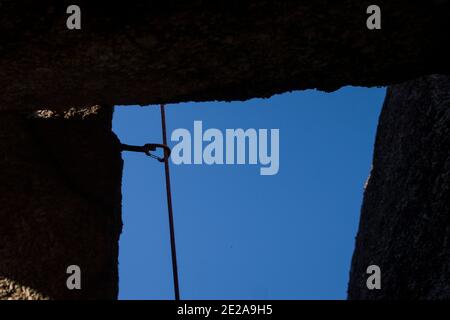 Moschettone di arrampicata su roccia che tiene su una corda in controluce dentro il mezzo delle rocce Foto Stock