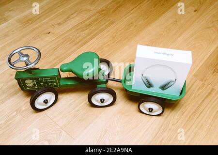 Parigi, Francia - 7 gennaio 2020: Vista dall'alto del giocattolo verde Kid bambino trattore con Apple Computers AirPods Max cuffie sovrauricolari nel bagagliaio della carrozza Foto Stock