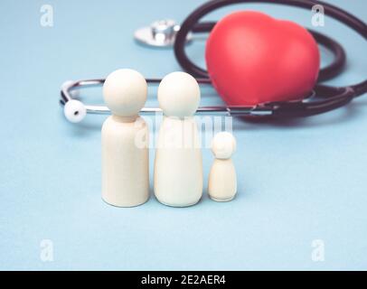 famiglia di figure in legno di uomini sullo sfondo di cuore rosso e stetoscopio, concetto di assicurazione sanitaria, primo piano Foto Stock