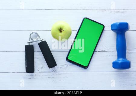 smartphone con attrezzature sportive su sfondo in legno bianco Foto Stock
