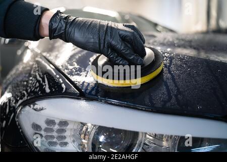 L'uomo pulisce il cofano dell'auto con una spugna circolare. Preparazione automatica per la lucidatura. Lavaggio dettagliato dell'auto Foto Stock