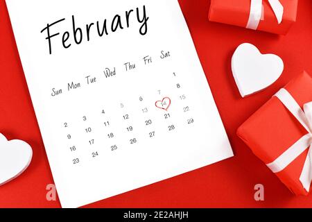 Primo piano del foglio del calendario di febbraio con San Valentino in data il 14 segnato con cuore rosso circondato da scatole regalo e cuore su sfondo rosso Foto Stock