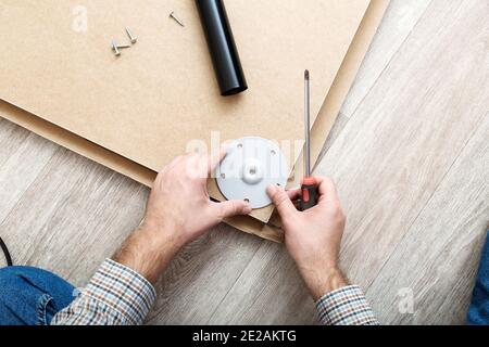 Montaggio di mobili con un cacciavite. Il padrone delle mani maschili raccoglie i mobili usando gli attrezzi del cacciavite, lo strumento a casa. In movimento, miglioramento domestico Foto Stock