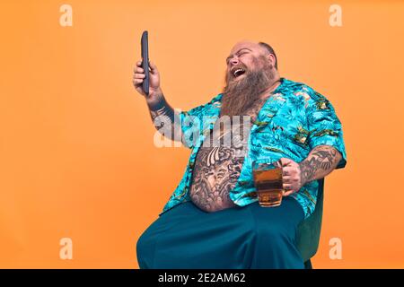 Uomo che guarda la televisione mentre beve e mangia. Divertente ritratto dell'uomo hipster su uno sfondo colorato Foto Stock