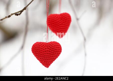 Cuori di amore appesi su un ramo di albero su sfondo bianco nevoso. Due simboli di San Valentino in maglia rossa nella foresta invernale, sfondo per le vacanze Foto Stock