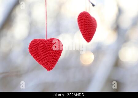 Cuori di San Valentino appesi su un ramo di albero nella foresta invernale. Due cuori di colore rosso in maglia alla luce del sole, simbolo di amore romantico, sfondo per le vacanze Foto Stock