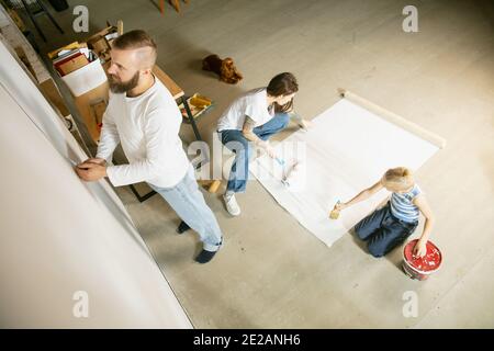 Giovane coppia, famiglia che ripara insieme l'appartamento. Madre, padre e figlio che fanno il makeover domestico o il rinnovamento. Concetto di relazioni, movimento, amore. Preparazione dello sfondo per la visualizzazione Foto Stock