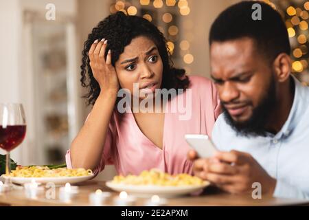 Donna nera arrabbiata guardando il ragazzo, uomo che usa il telefono Foto Stock