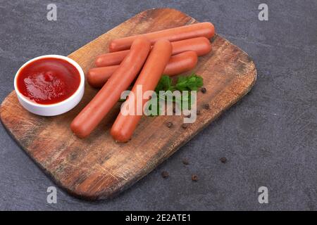Salsicce di frankfurter crude con ketchup sul tagliere Foto Stock