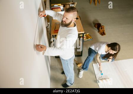 Giovane coppia, famiglia che ripara insieme l'appartamento. Uomo e donna sposati che fanno il makeover o la ristrutturazione della casa. Concetto di relazioni, movimento, amore. Preparazione dello sfondo per la visualizzazione Foto Stock