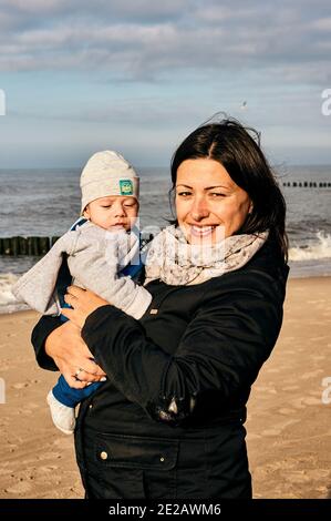 SARBINOWO, POLONIA - 15 ottobre 2017: Donna caucasica polacca felice che tiene un bambino piccolo ragazzo in spiaggia in una giornata nuvolosa Foto Stock