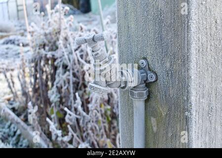 primo piano del rubinetto d'acqua esterno coperto di ghiaccio collegato ad un palo di legno su un giardino di assegnazione in inverno Foto Stock