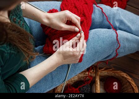 Giovane donna che lavora a maglia rosso silenziatore a casa nel tempo libero, fancywork e concetto di lavoro al ago, primo piano del lavoro a mano, spazio di copia, dall'alto vista Foto Stock