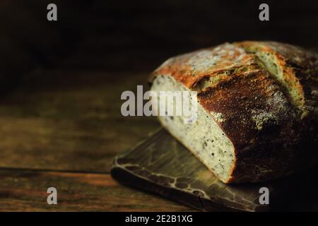 Una pagnotta di pane rotondo fatto in casa su uno sfondo scuro con spazio da copiare. Dolci privi di lievito con i propri cereali. Foto Stock