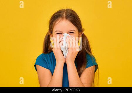 Bambina che soffia il naso nel fazzoletto bianco su sfondo giallo. Il bambino ha un raffreddore e un'influenza Foto Stock