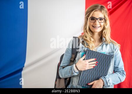 Giovane studente con parentesi graffe tiene libro di testo davanti alla bandiera della Francia. Foto Stock