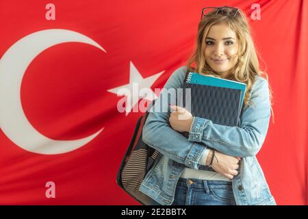 Bella studentessa sorride tenendo materiali di studio con una bandiera di Turchia dietro di lei. Foto Stock