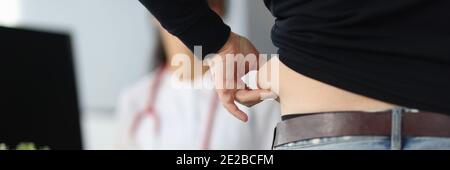 Paziente che tiene la piega grassa sullo stomaco con la mano nei medici primo piano dell'ufficio Foto Stock