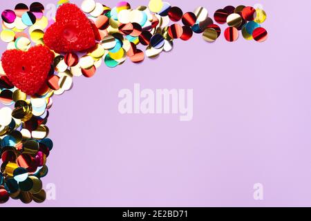 Confetti colorati e candele profumate a forma di cuore su sfondo viola con spazio vuoto. Foto Stock