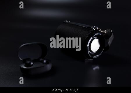 Cuffie wireless nere e altoparlante wireless su sfondo nero. Foto Stock