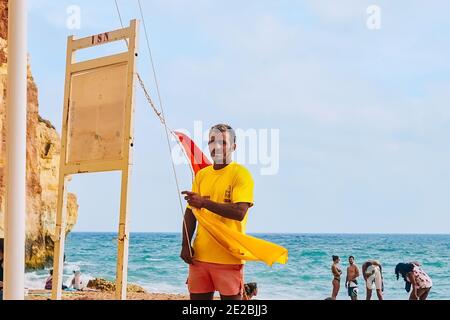 Benagil, Portogallo - 05/19/2020: Onde sulla spiaggia di Benagil in Portogallo. Molte persone nuotano e si abbronzano durante una tempesta. bagnino da spiaggia appende una bandiera Foto Stock