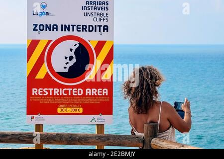 Benagil, Portogallo - 04/13/2020: Una donna si trova dietro una recinzione vicino a una scogliera e tiene un telefono tra le mani. Pericolo durante lo scatto delle foto Foto Stock