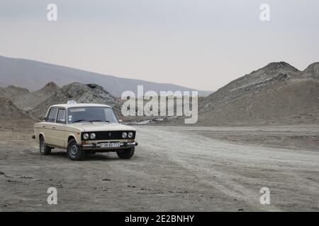 Auto vecchia Lada nel paesaggio estremo del deserto con vulcani di fango nel Parco Nazionale di Gobustan in Azerbaigian. Foto Stock