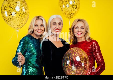 Bella donna anziana che fa festa e festeggia il nuovo anno. Donne di mezza età che indossano eleganti abiti scintillanti e si divertono. Ritratti in studio Foto Stock