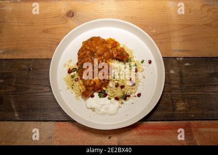 Un delizioso piatto di lento cotto sciogliere in bocca pollo tagine, con couscous e melograno su una rustica cucina in legno piano di lavoro. Foto Stock