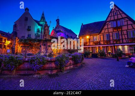 La piazza principale del villaggio feudale di Eguisheim con case a graticcio, vecchia fontana e una chiesa. Foto scattata il 10 agosto 2019 nell'es Foto Stock