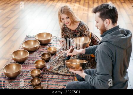 Donna e uomo che giocano su una ciotola di canto tibetiano per terapia audio seduta nello studio di yoga Foto Stock