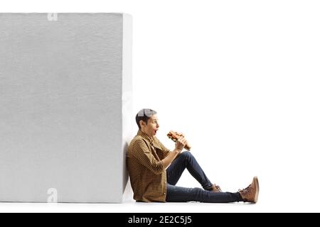 Eccitato giovane uomo che mangia un panino baguette e si appoggia a parete isolata su sfondo bianco Foto Stock