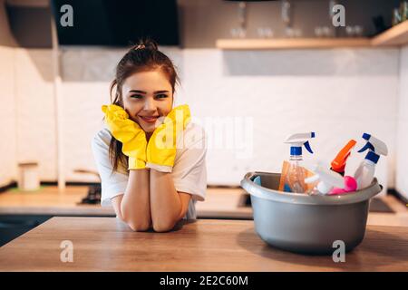 Bella donna in guanti protettivi gialli è sorridente in cucina durante la pulizia Foto Stock