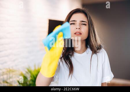 Donna in guanti protettivi gialli pulendo e pulendo la polvere in casa sua, primo piano. Foto Stock