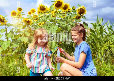 Due bambini sorridenti felici nel campo di girasoli ridono e soffiano bolle. Estate nel villaggio. Foto Stock