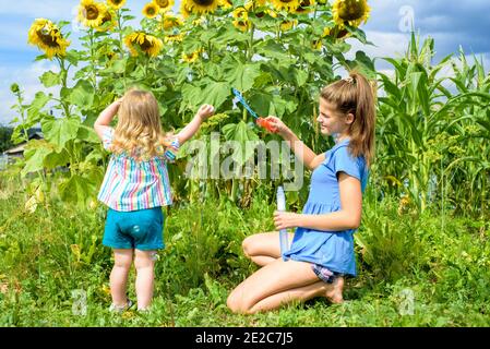 Due bambini sorridenti felici nel campo di girasoli ridono e soffiano bolle. Estate nel villaggio. Foto Stock