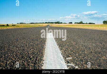 Strada asfaltata all'orizzonte.campi verdi estivi. Cielo blu senza nuvole Foto Stock