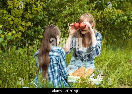 Felice donna sorridente e divertimento godendo capretto, madre che tiene le mele rosse vicino agli occhi.picnic nel parco, famiglia felice. Soleggiato giorno estivo all'aperto Foto Stock