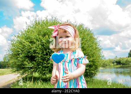 bambina con lollipop nel parco soleggiato. Bambini i bambini giocano all'aperto in estate, mangiano i dolci. Bimbo con snack dolce. Capretto con il delizia dello zucchero. Foto Stock