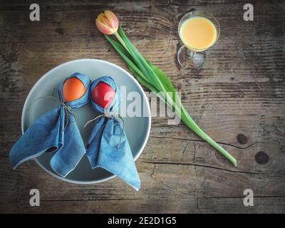 Bambole realizzate con uova colorate e tovaglioli su piatto blu. Tulipano e bicchiere di uovo di nog su tavolo di legno. Decorazione di Pasqua. Foto a soffitto con spazio per la copia. Foto Stock