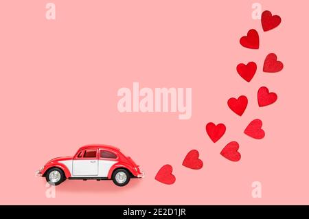 Fulda, Germania - DEC 18, 2020: Piccola auto giocattolo retrò con molti cuori rossi per San Valentino su sfondo rosa. Amore e tema di vacanza. Compleanno e va Foto Stock