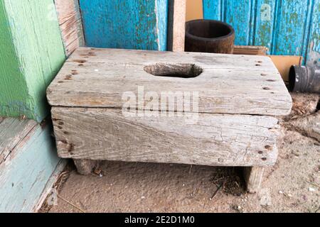 Sgabello di legno dilatato con un foro nella seduta area sul pavimento in cemento vicino alla casa del paese Foto Stock