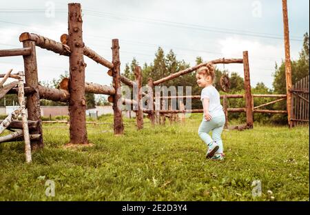 Stile di vita, bambina che corre circa la recinzione di legno, giorno d'estate sullo sfondo della foresta. Vocazione nel villaggio. Sole e tramonto. Foto Stock